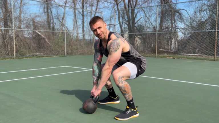 Fit man squatting and holding Kettlebell in his hands, preparing to do a Kettlebell Swing ecercise